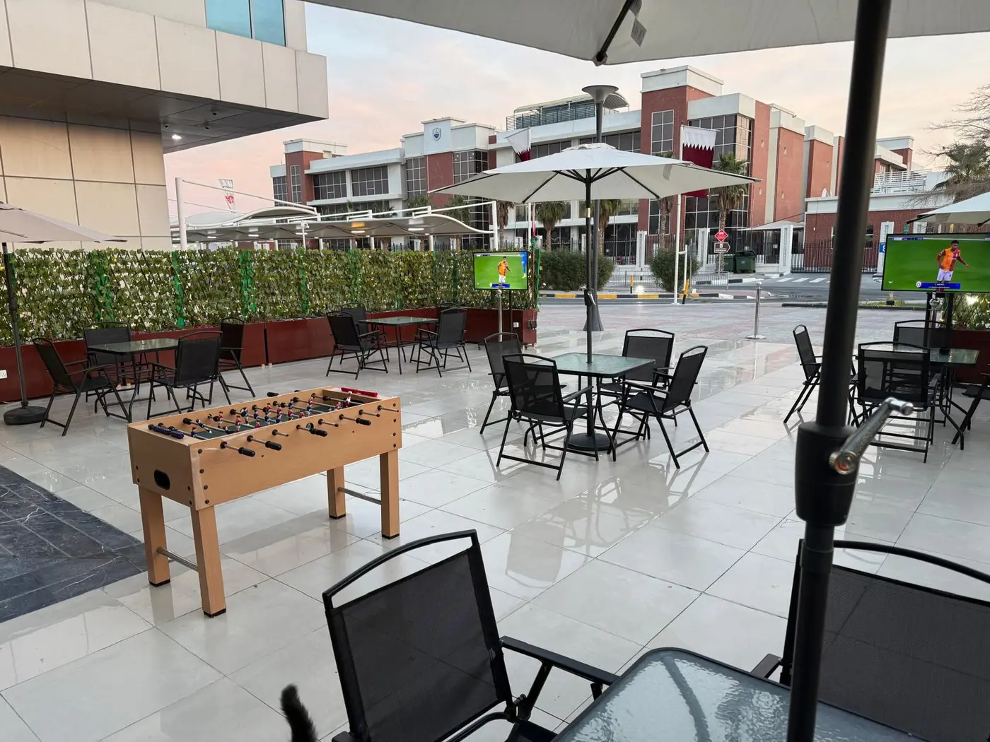 Outdoor terrace at Al Thumama Mall with tables, umbrellas, a foosball table and screens